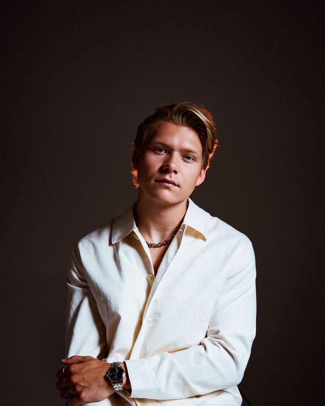 Adam Woods seated against a dark brown backdrop in a cream shirt