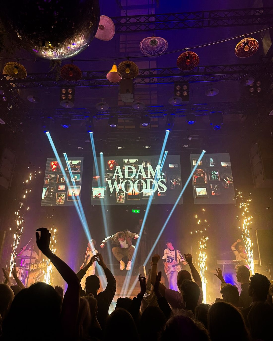 Adam Woods mid-jump on stage with pyrotechnics and a full crowd