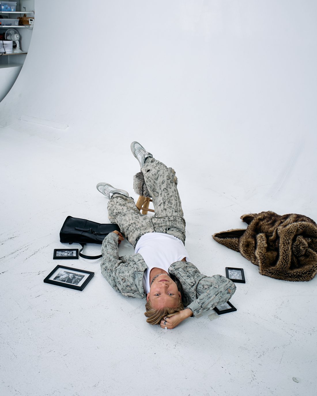 Adam Woods lying on a white studio floor surrounded by framed photographs