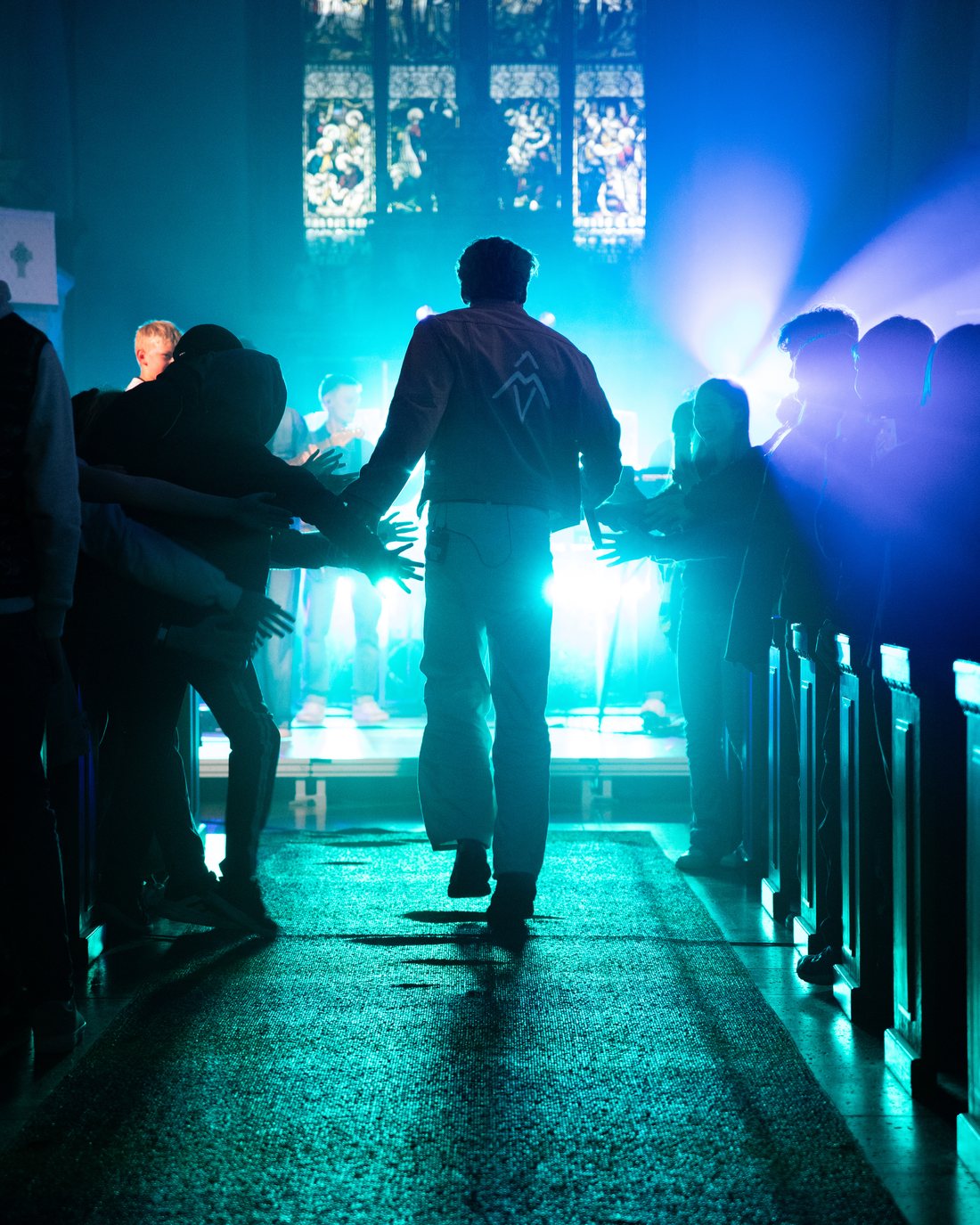 Adam Woods walking towards a blue-lit stage past the audience